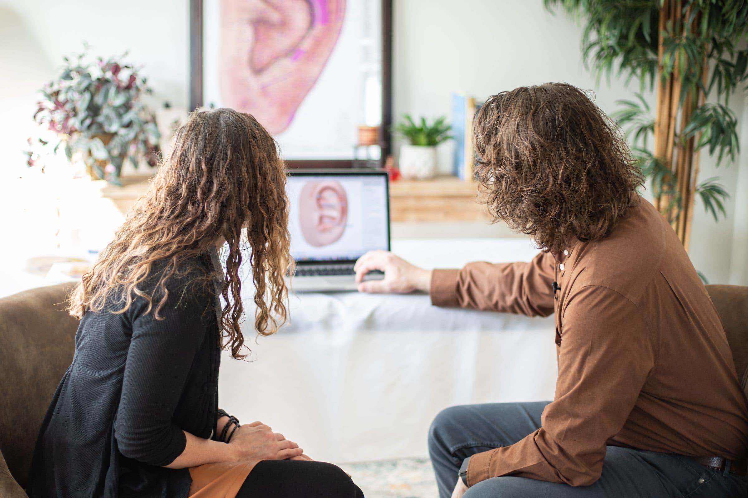 Two people looking at Auriculo 360 on a laptop, one pointing at the ear on the screen.